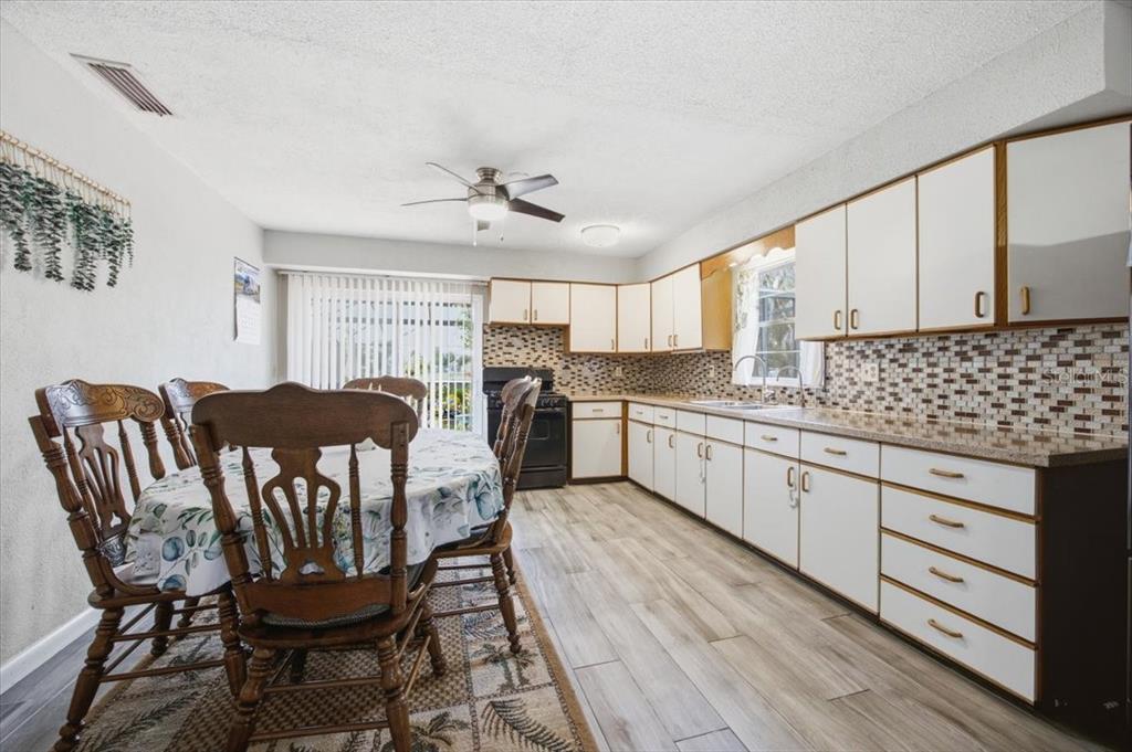 A kitchen and dining area with white cabinets, tile backsplash, and wood-look flooring — 2266 LAKE LIZZIE COURT, ST CLOUD, FL