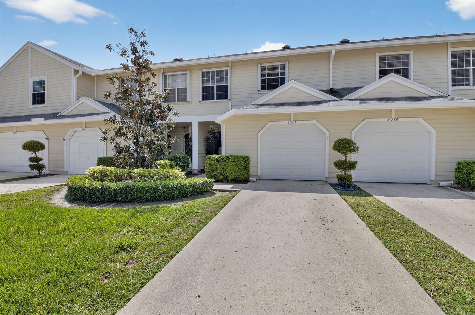 A row of beige townhouses with attached garages and manicured landscaping under a blue sky — 5282 Sapphire Valley, Boca Raton FL 33486, BOCA RATON, FL