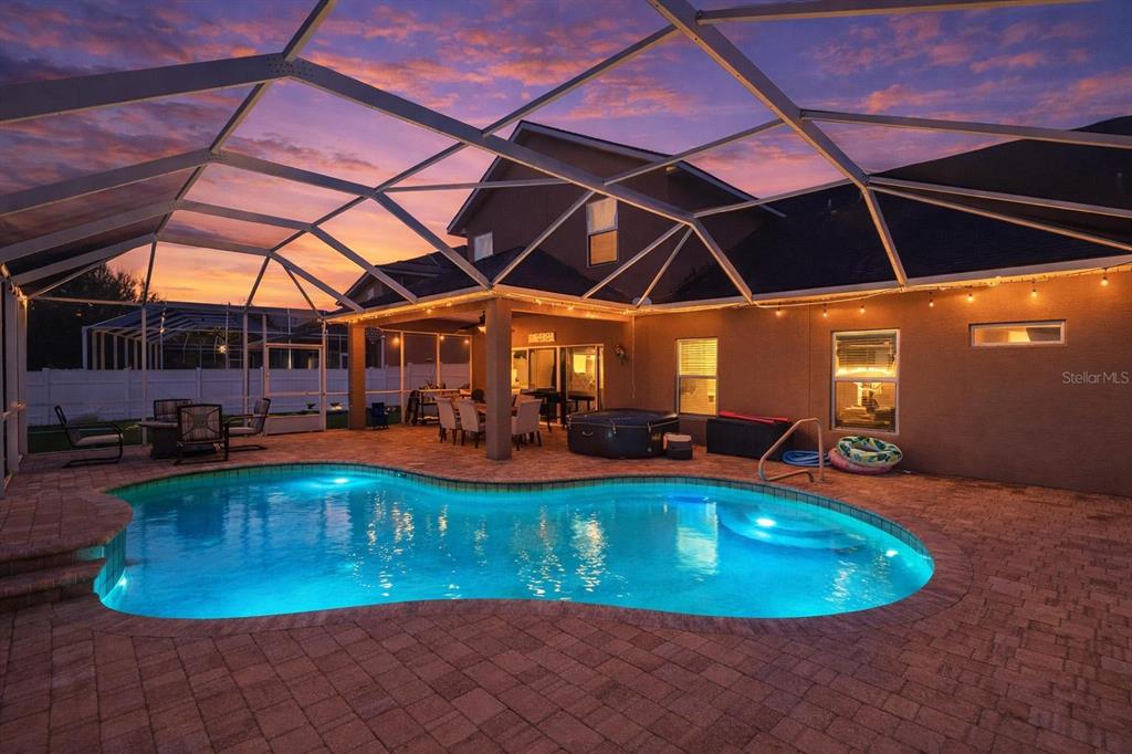A backyard swimming pool with a screened-in patio and outdoor seating at sunset — 6970 VINTAGE LANE, PORT ORANGE, FL
