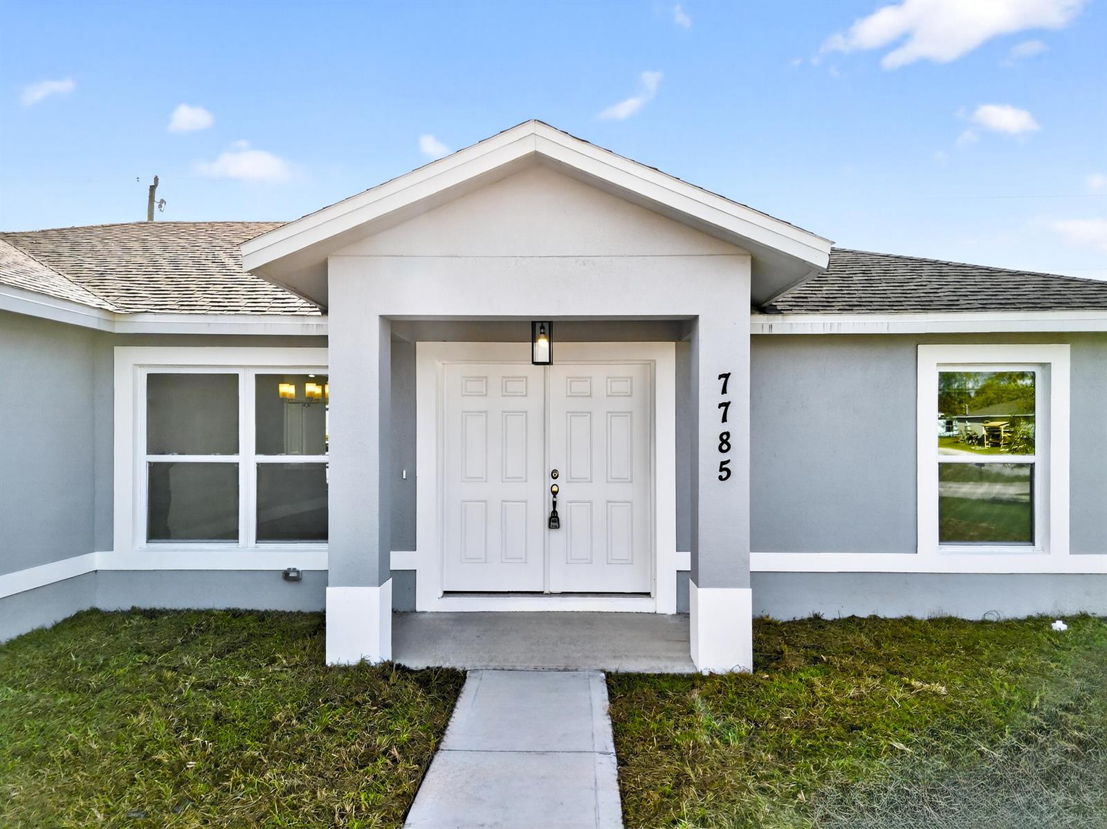 The exterior of a gray house features a white double front door and a concrete walkway — 7785 105th Avenue, Vero Beach FL 32967, VERO BEACH, FL