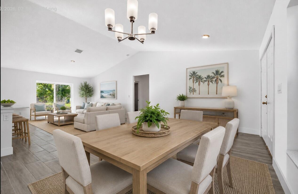 A dining area with a wooden table and chairs opens into a bright living room — 7785 105th Avenue, Vero Beach FL 32967, VERO BEACH, FL