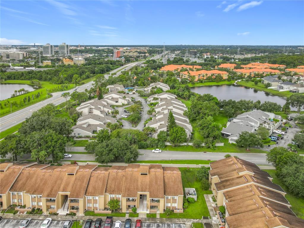 An aerial view of a residential townhouse complex with multiple buildings, parking, and a lake — 5249 VINELAND ROAD, ORLANDO, FL