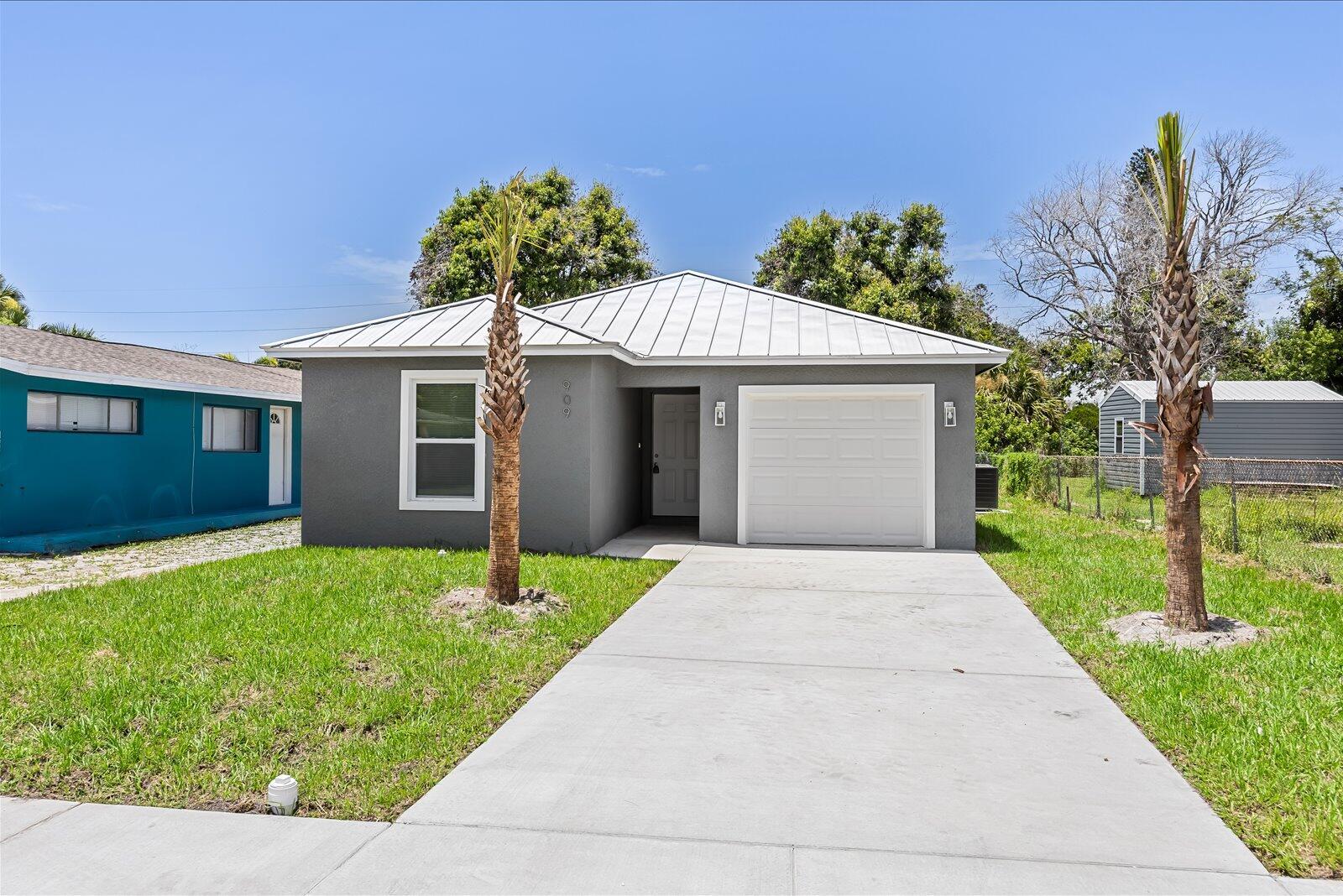 A gray single-story house with a white metal roof and a concrete driveway — 909 20TH N, Fort Pierce FL 34950, FORT PIERCE, FL