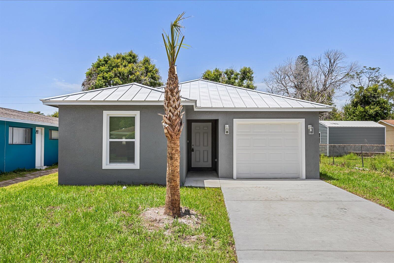 A gray single-story house with a metal roof, a front door, and a garage door — 909 20TH N, Fort Pierce FL 34950, FORT PIERCE, FL