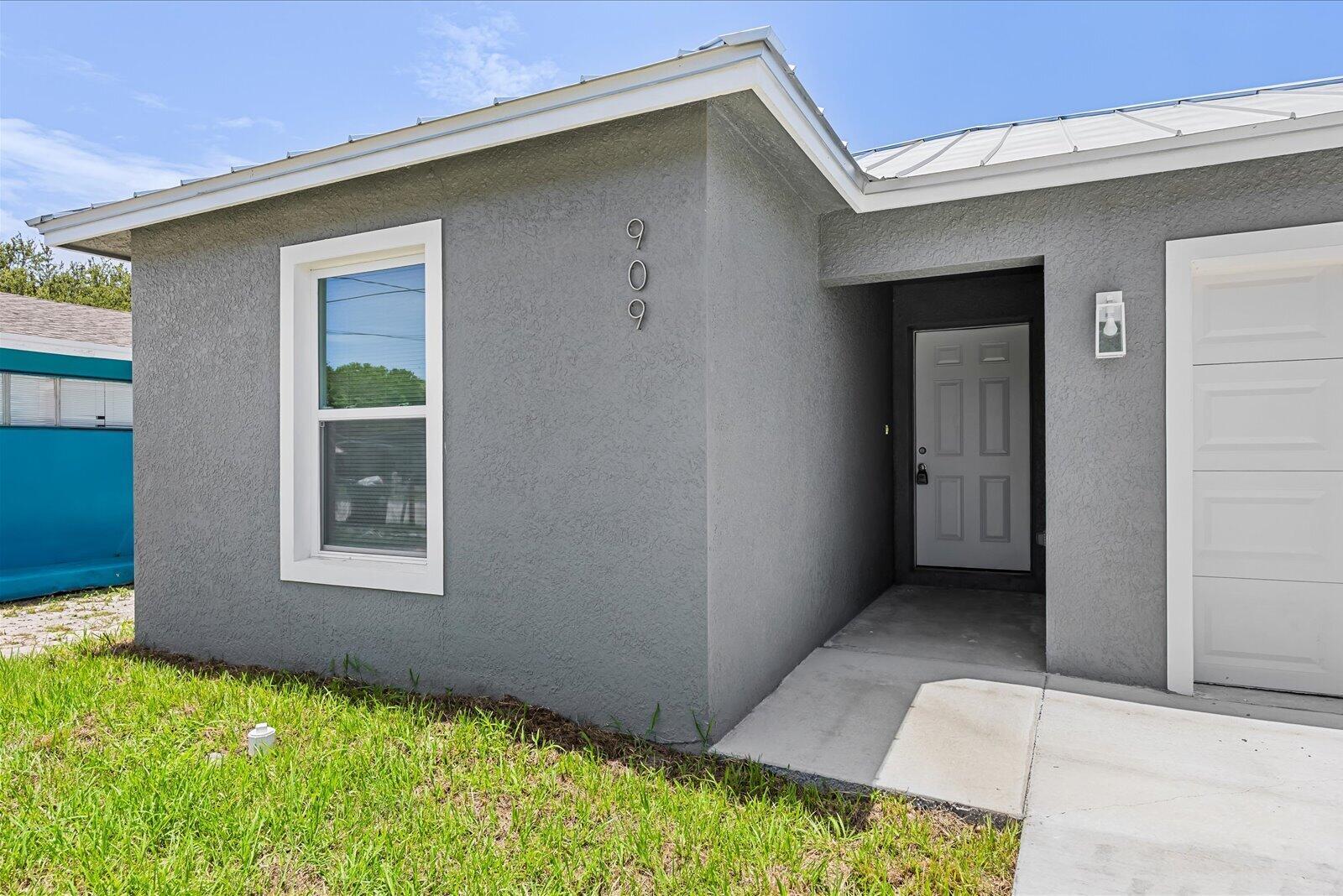 The exterior of a gray house features a white front door and a garage — 909 20TH N, Fort Pierce FL 34950, FORT PIERCE, FL