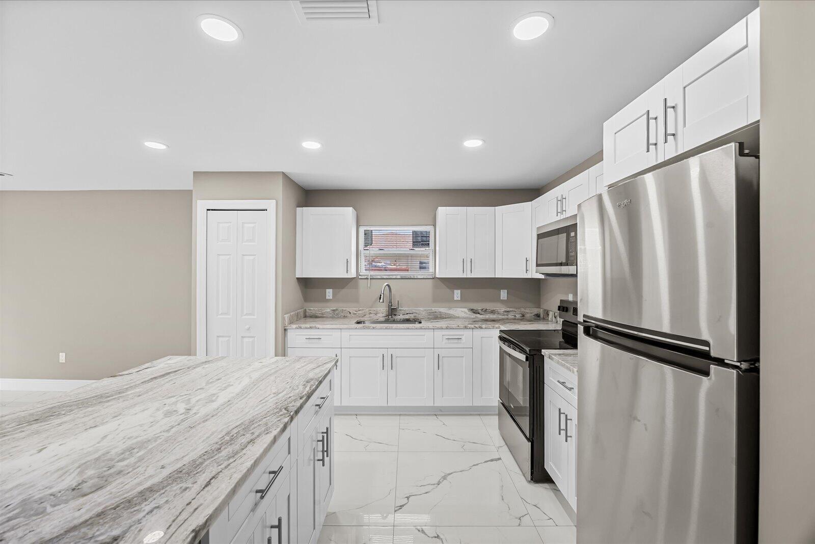 A modern kitchen features white cabinets, stainless steel appliances, and a marble-patterned island countertop — 909 20TH N, Fort Pierce FL 34950, FORT PIERCE, FL