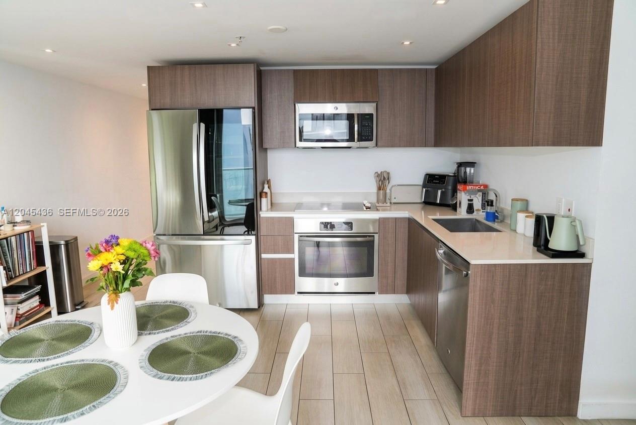 A modern kitchen features wood-grain cabinets, stainless steel appliances, and a white dining table — 1600 SW 1st Ave # 906, Miami FL 33129, MIAMI, FL