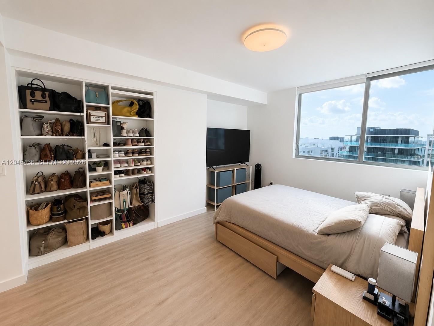 A bedroom features a built-in shelving unit, a bed, a television, and large windows — 1600 SW 1st Ave # 906, Miami FL 33129, MIAMI, FL