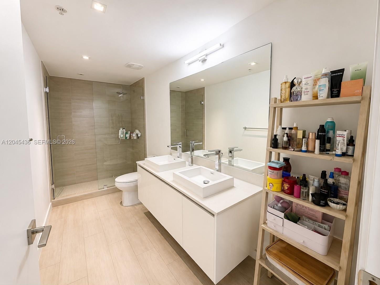 A modern bathroom features a double vanity, a glass-enclosed shower, and a wooden shelving unit — 1600 SW 1st Ave # 906, Miami FL 33129, MIAMI, FL