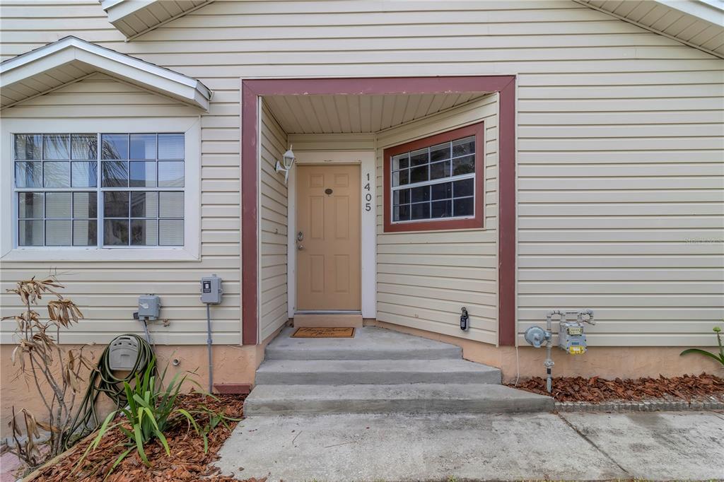The exterior of a house features beige siding, a tan front door, and concrete steps — 1405 CRICKET COURT, LONGWOOD, FL
