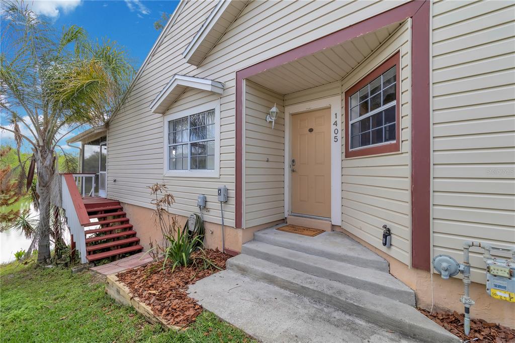 The exterior of a house features beige siding, a tan front door, and concrete steps — 1405 CRICKET COURT, LONGWOOD, FL