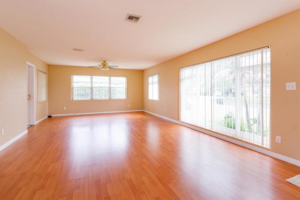 An empty living room features light-colored walls, wood-look flooring, a ceiling fan, and large windows — 1519 CATALPA LANE, ORLANDO, FL