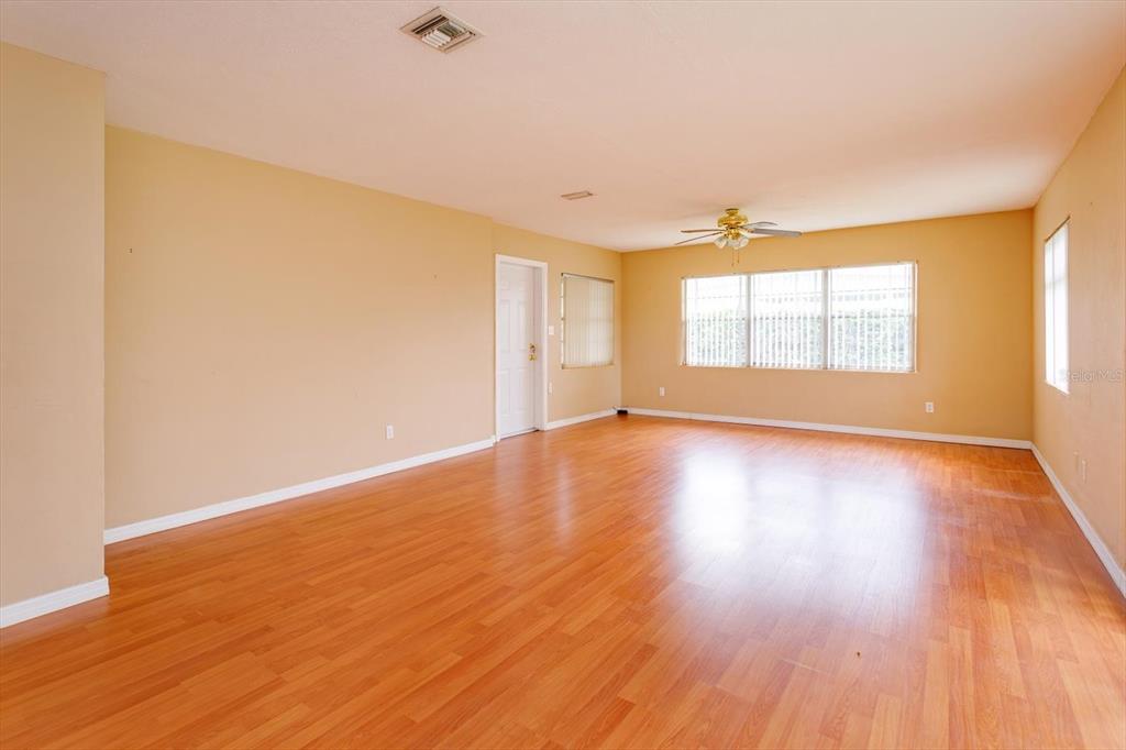 An empty room features light-colored walls, wood-look flooring, a ceiling fan, and large windows — 1519 CATALPA LANE, ORLANDO, FL