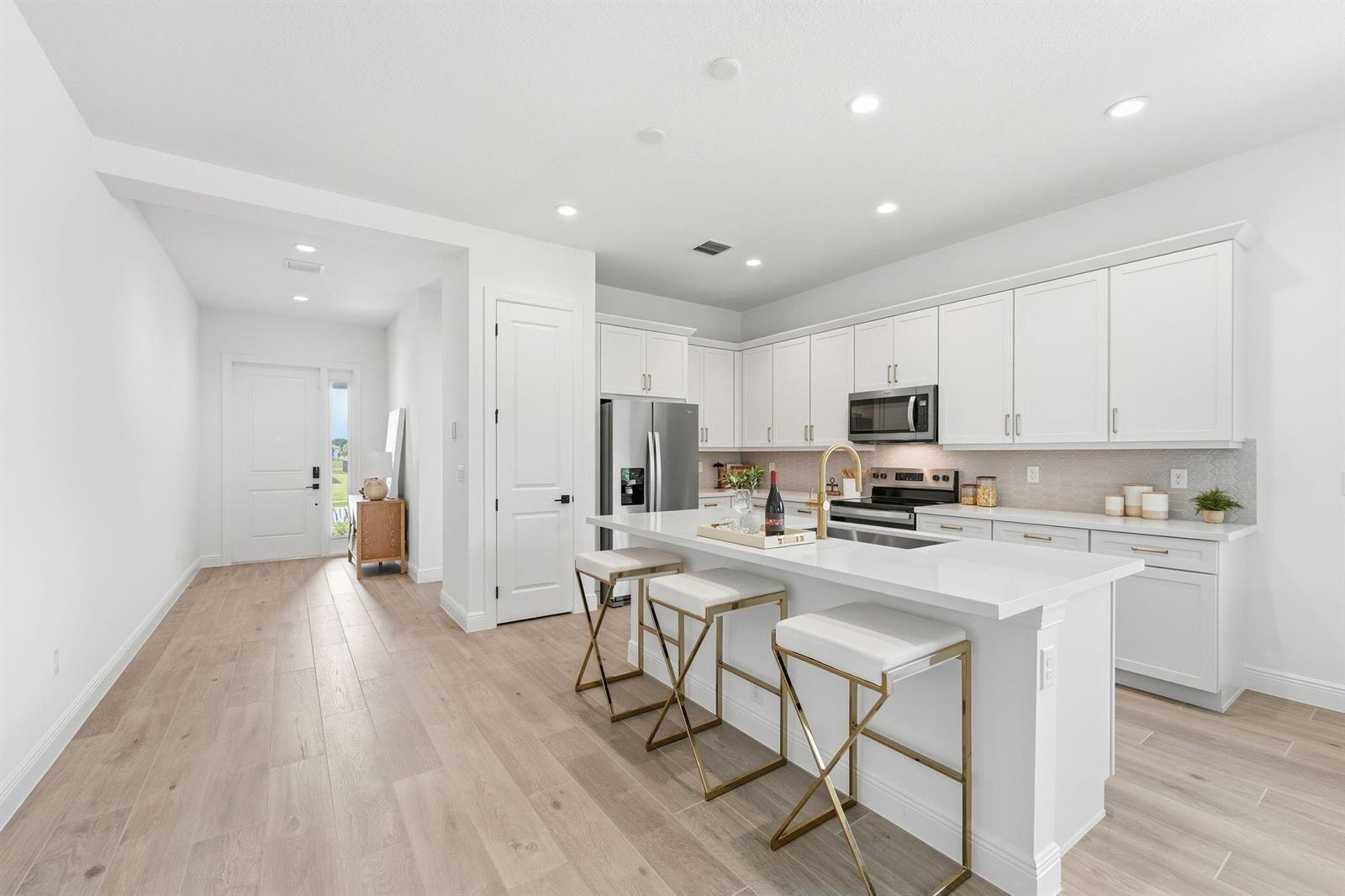 A modern kitchen features white cabinetry, a quartz island with gold barstools, and light flooring — 6783 68th Square, Vero Beach FL 32967, VERO BEACH, FL
