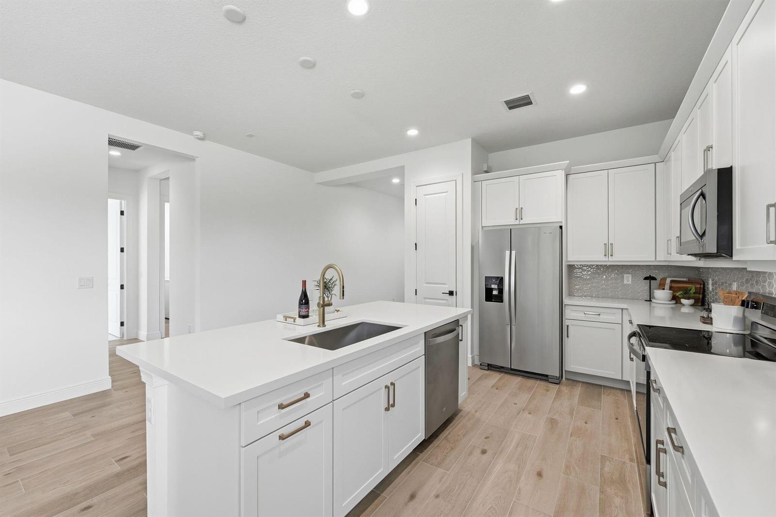A modern kitchen features white cabinetry, stainless steel appliances, and a central island with sink — 6783 68th Square, Vero Beach FL 32967, VERO BEACH, FL