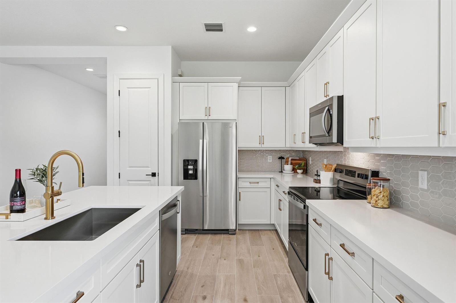 A modern kitchen features white cabinetry, stainless steel appliances, a quartz island, and gold hardware — 6783 68th Square, Vero Beach FL 32967, VERO BEACH, FL