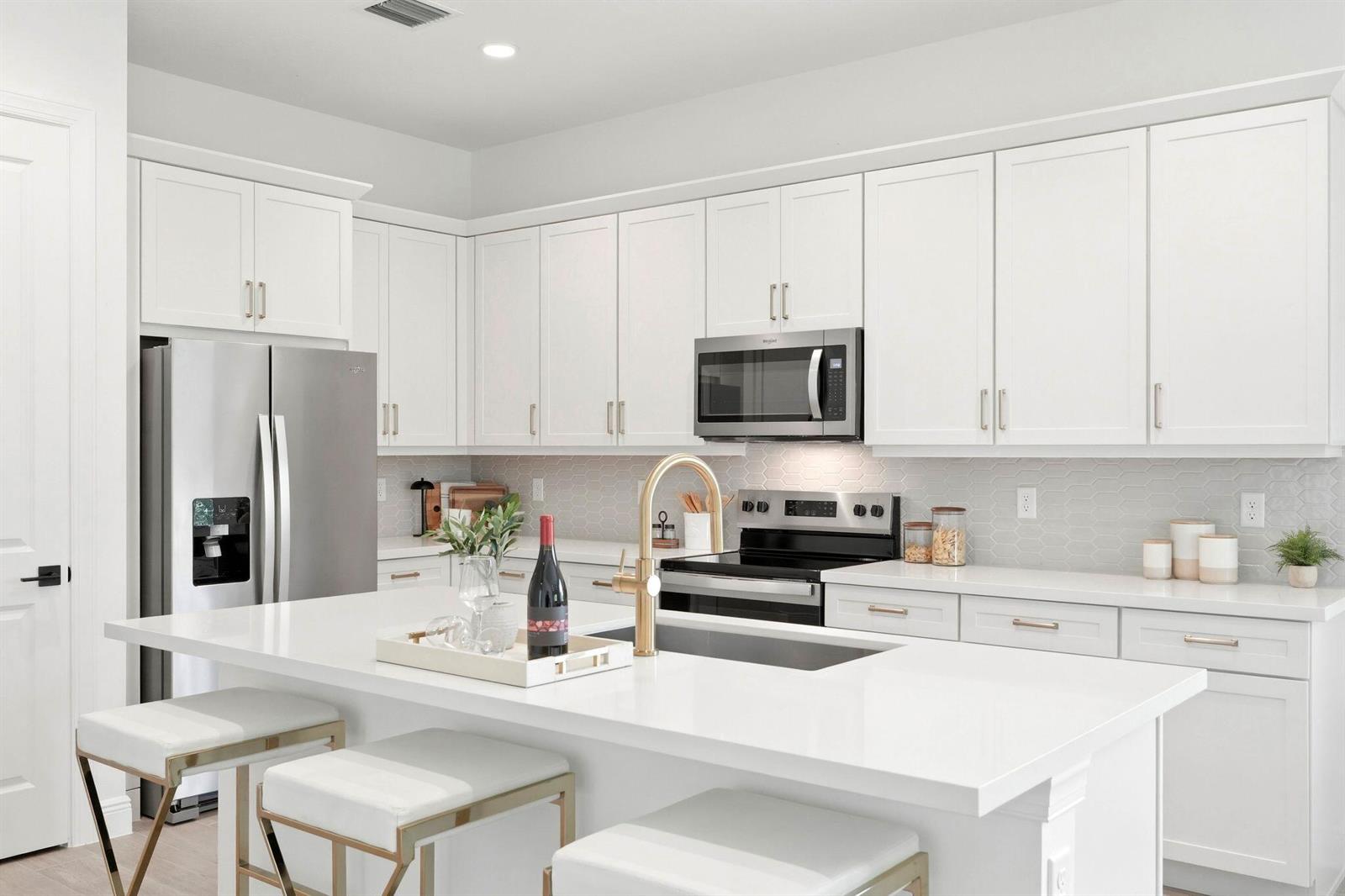 A modern white kitchen features a large island, stainless steel appliances, and gold-toned hardware — 6783 68th Square, Vero Beach FL 32967, VERO BEACH, FL
