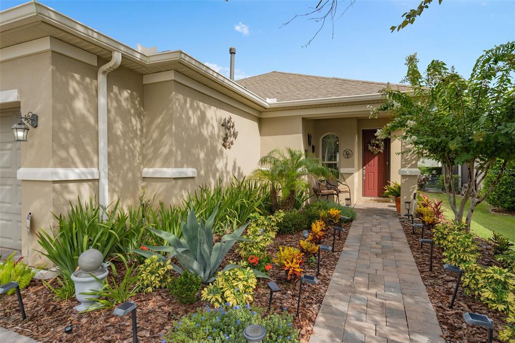 A paved walkway leads to the front entrance of a tan house with landscaped gardens — 2594 STARGRASS CIRCLE, CLERMONT, FL