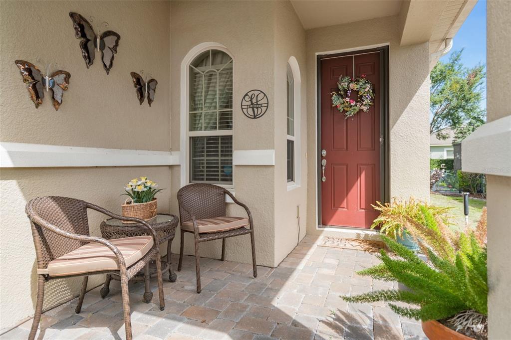 A covered front porch features two wicker chairs, a small table, and a red door — 2594 STARGRASS CIRCLE, CLERMONT, FL