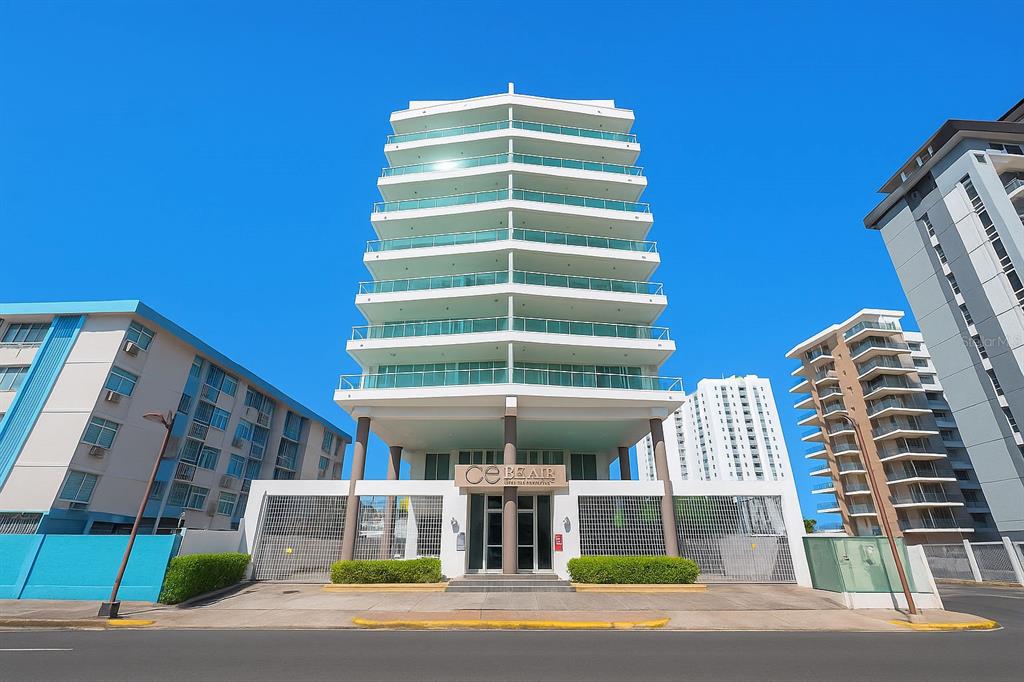 A modern white high-rise building with glass balconies stands above a gated ground-level entrance — 5575 AVENIDA ISLA VERDE UNIT 903, CAROLINA, PR