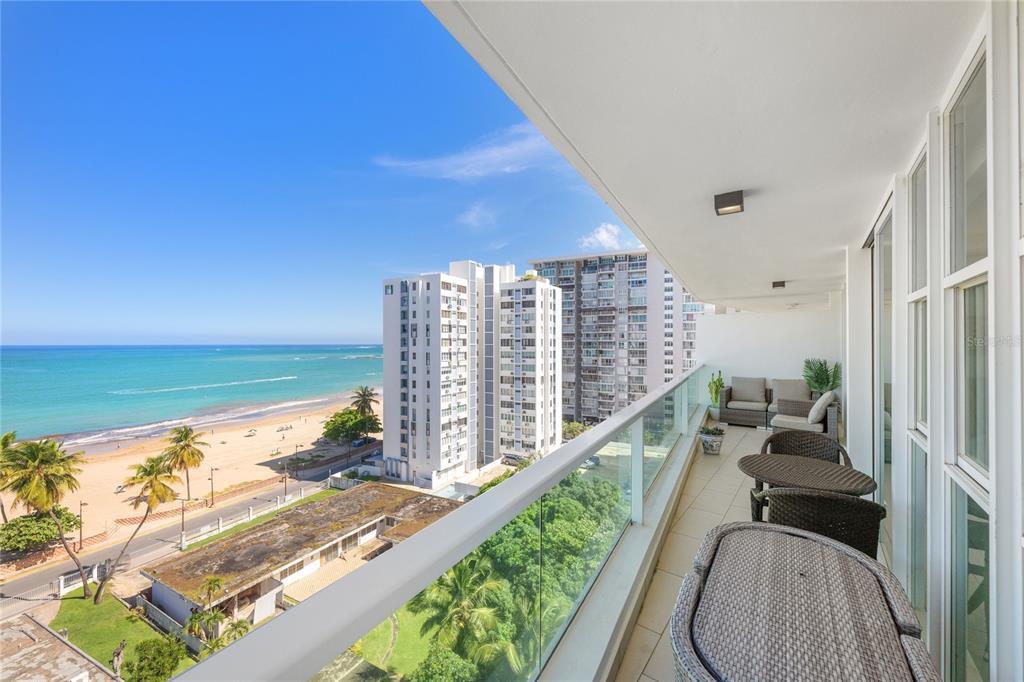 A balcony with outdoor furniture overlooks a beach, the ocean, and nearby high-rise buildings — 5575 AVENIDA ISLA VERDE UNIT 903, CAROLINA, PR