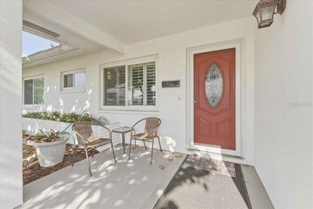 A covered porch features a red front door, two chairs, and a small table — 9875 MAINLANDS BOULEVARD W, PINELLAS PARK, FL