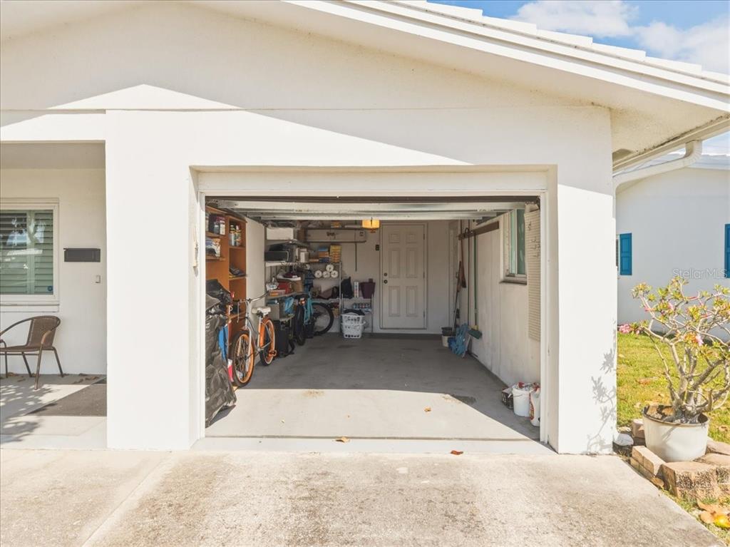 An open garage with a concrete floor, storage shelving, bicycles, and a white entry door — 9875 MAINLANDS BOULEVARD W, PINELLAS PARK, FL