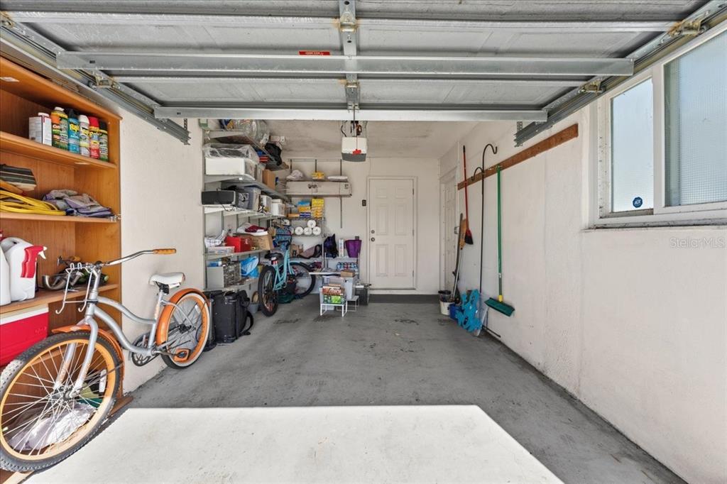 A garage features concrete floors, open shelving, a bicycle, and a white entry door — 9875 MAINLANDS BOULEVARD W, PINELLAS PARK, FL