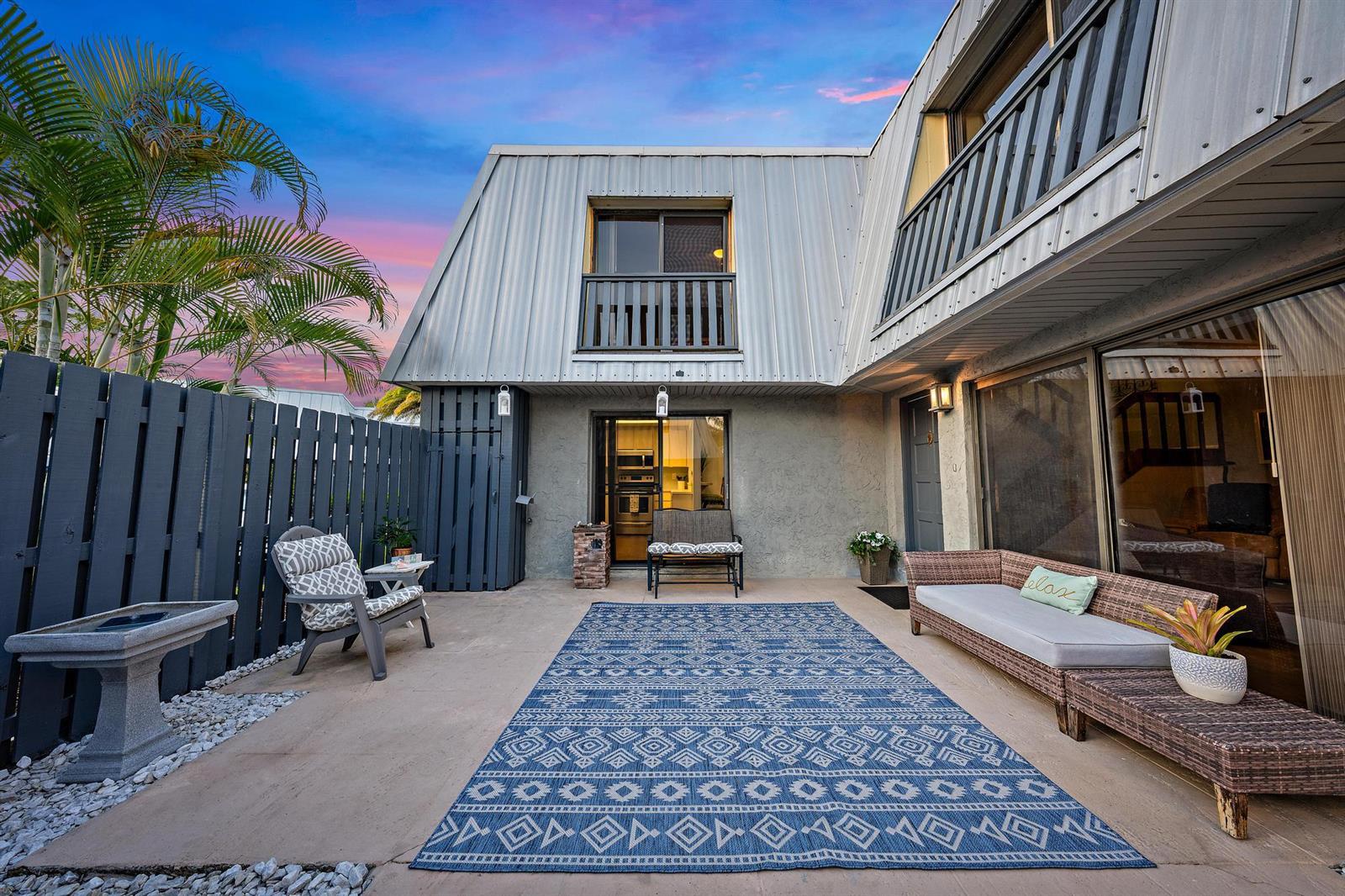 A patio with a blue patterned rug, outdoor furniture, and a metal-sided two-story building exterior — 3840 SE Jefferson Street, Stuart FL 34997, STUART, FL