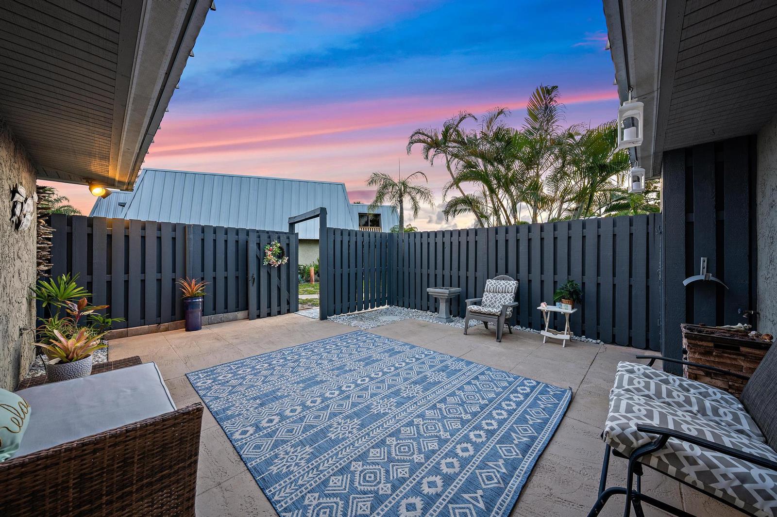A patio features a blue patterned rug, outdoor furniture, and a dark wooden privacy fence — 3840 SE Jefferson Street, Stuart FL 34997, STUART, FL