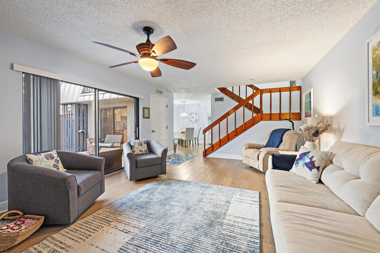 A living room features a ceiling fan, wooden staircase, sliding glass doors, and light flooring — 3840 SE Jefferson Street, Stuart FL 34997, STUART, FL