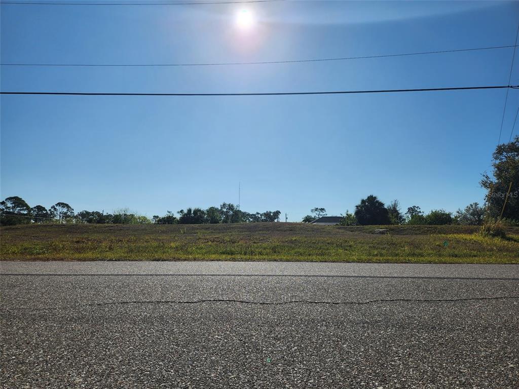 A view from a paved road looking toward a vacant, grassy lot under a bright sun — 155 JADE STREET, ROTONDA WEST, FL