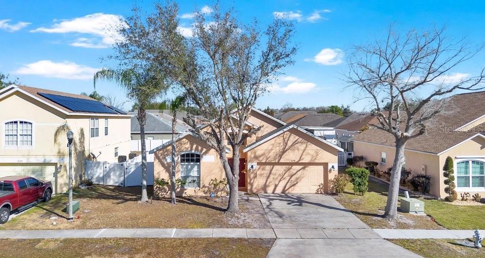 A two-story suburban house with a tan stucco exterior, a two-car garage, and mature trees — 2109 WOODSEDGE DRIVE, KISSIMMEE, FL