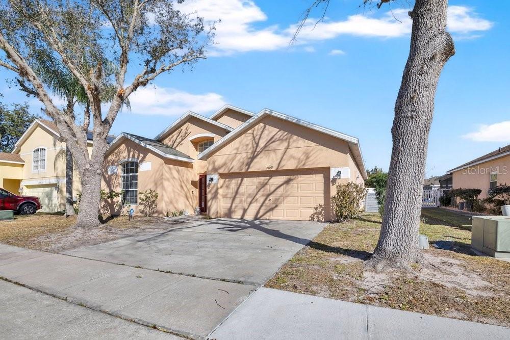 A tan, single-story suburban house with a two-car garage and a concrete driveway — 2109 WOODSEDGE DRIVE, KISSIMMEE, FL