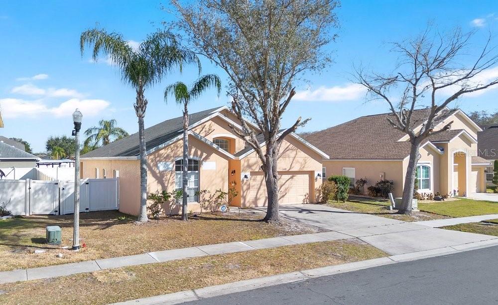 A single-story peach-colored house with a two-car garage and palm trees in the front yard — 2109 WOODSEDGE DRIVE, KISSIMMEE, FL