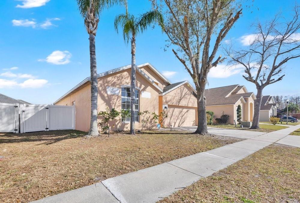 A single-story peach-colored house with a two-car garage, palm trees, and a white fence — 2109 WOODSEDGE DRIVE, KISSIMMEE, FL