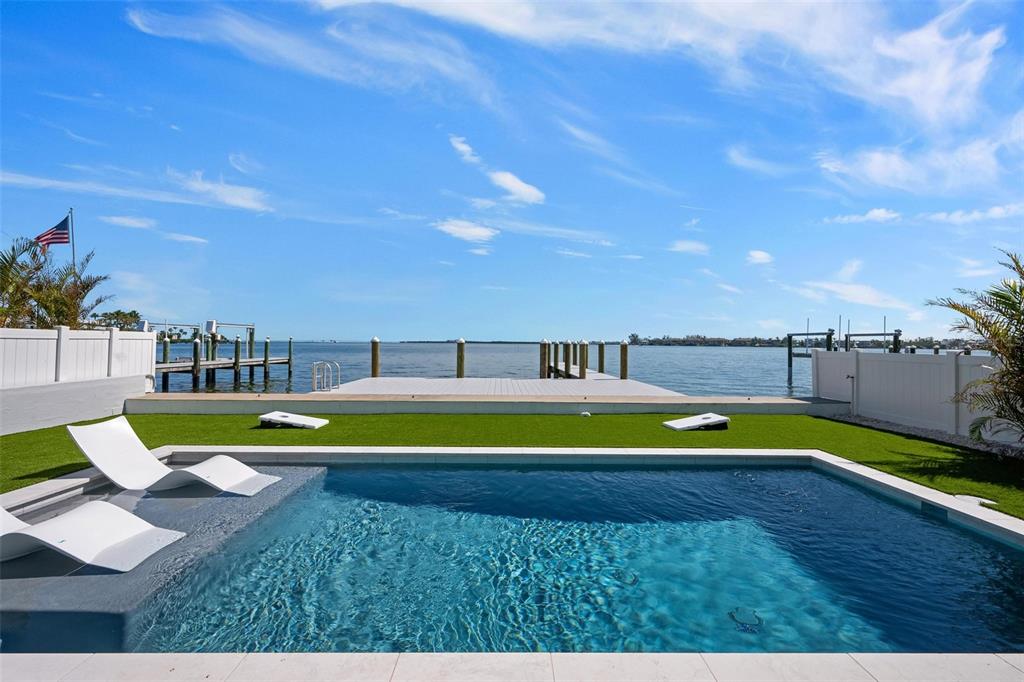 A swimming pool with lounge chairs sits in a backyard overlooking a waterfront dock — 118 9TH STREET N, BRADENTON BEACH, FL