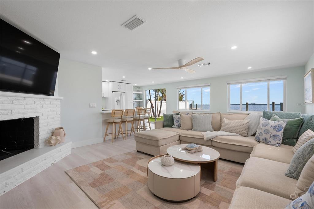 A living room with a white brick fireplace, sectional sofa, and water views through windows — 118 9TH STREET N, BRADENTON BEACH, FL