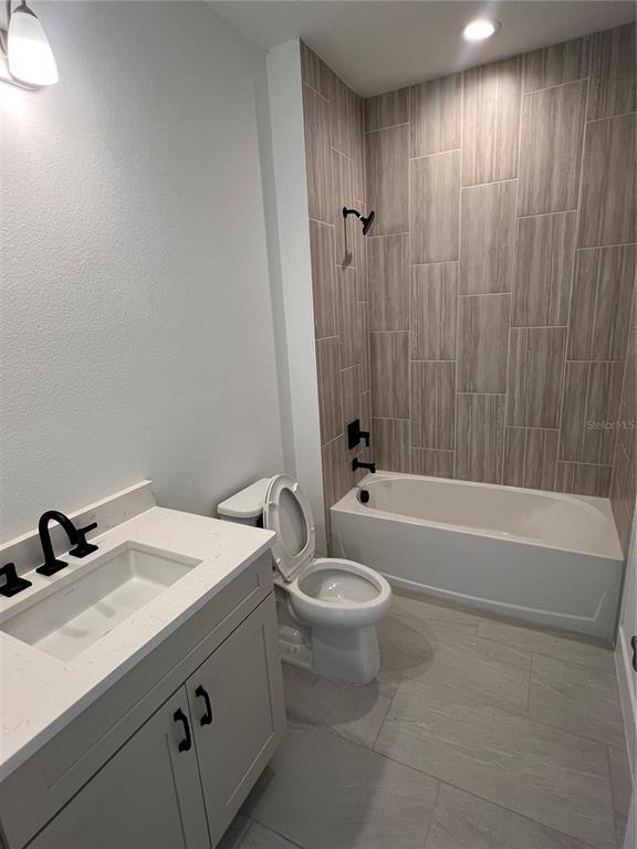 A bathroom features a white vanity, a toilet, and a bathtub with wood-look tile walls — 1605 STONECLIFF DRIVE, APOPKA, FL