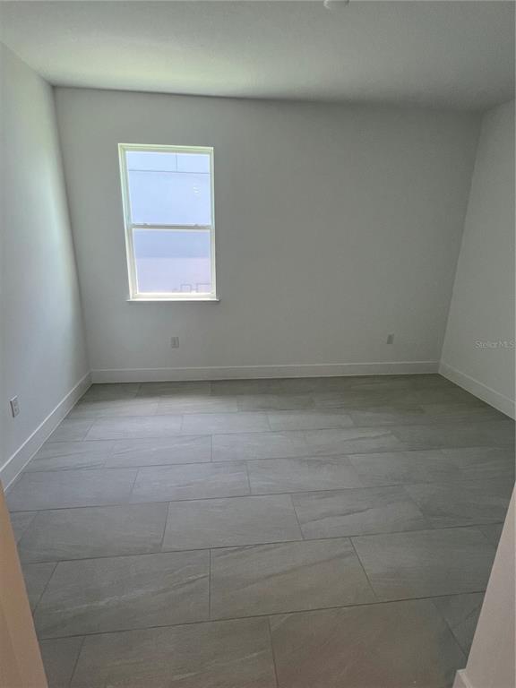 An empty room with gray tile flooring and a single window on the back wall — 1605 STONECLIFF DRIVE, APOPKA, FL