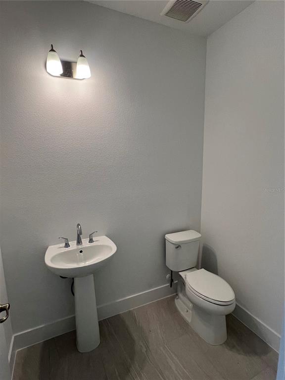 A small bathroom features a white pedestal sink, a toilet, and light-colored tile flooring — 1605 STONECLIFF DRIVE, APOPKA, FL