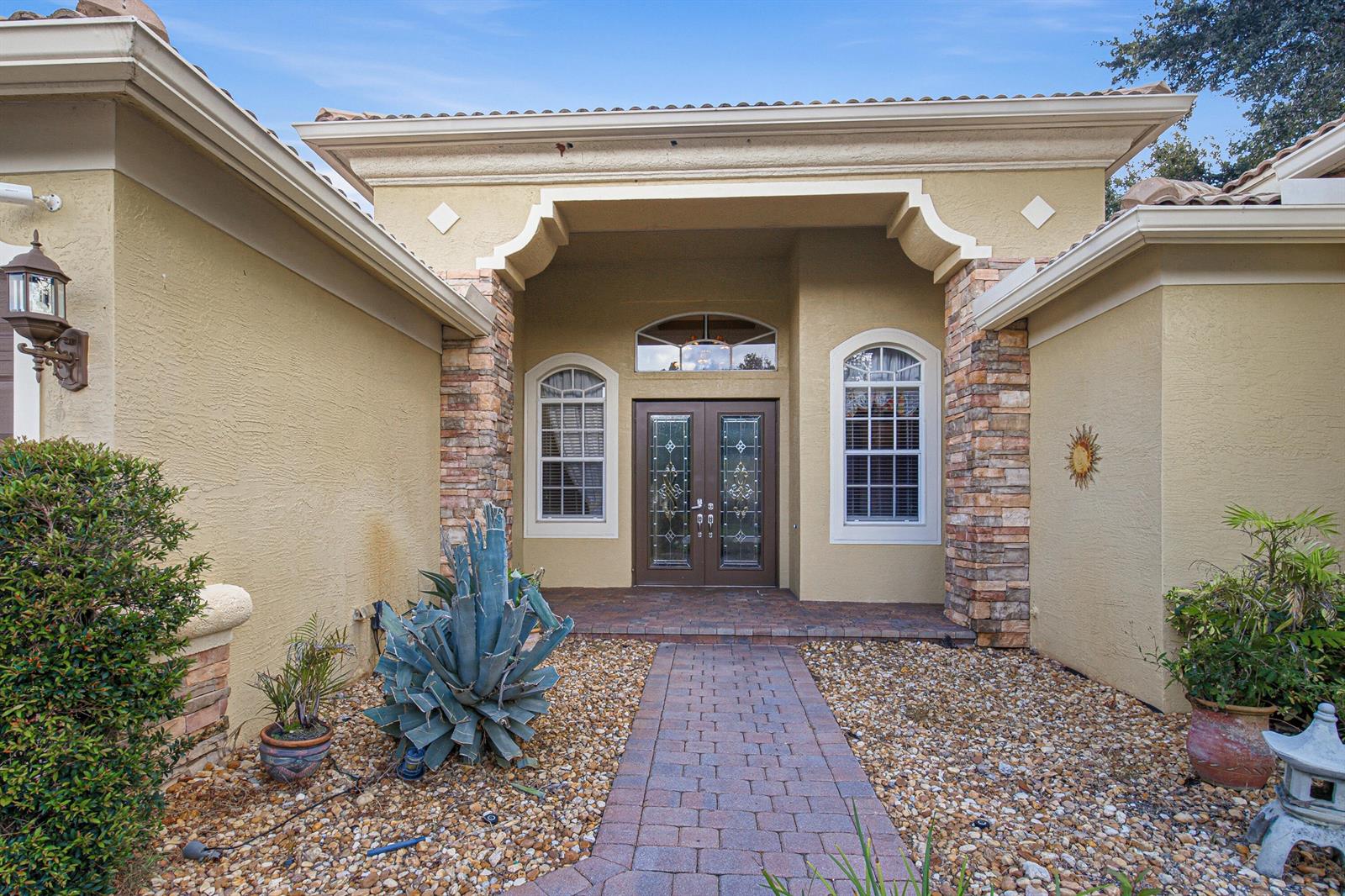 The exterior of a house features a stone-accented entryway, double glass doors, and a walkway — LAKE WORTH, FL