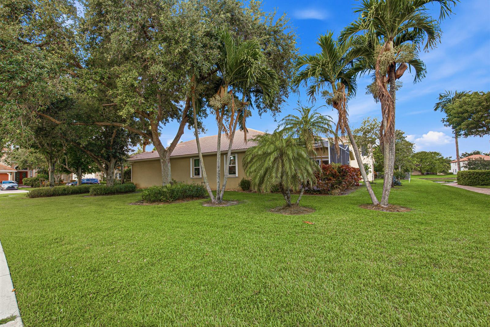 A tan house with a tiled roof sits behind a large lawn and palm trees — LAKE WORTH, FL