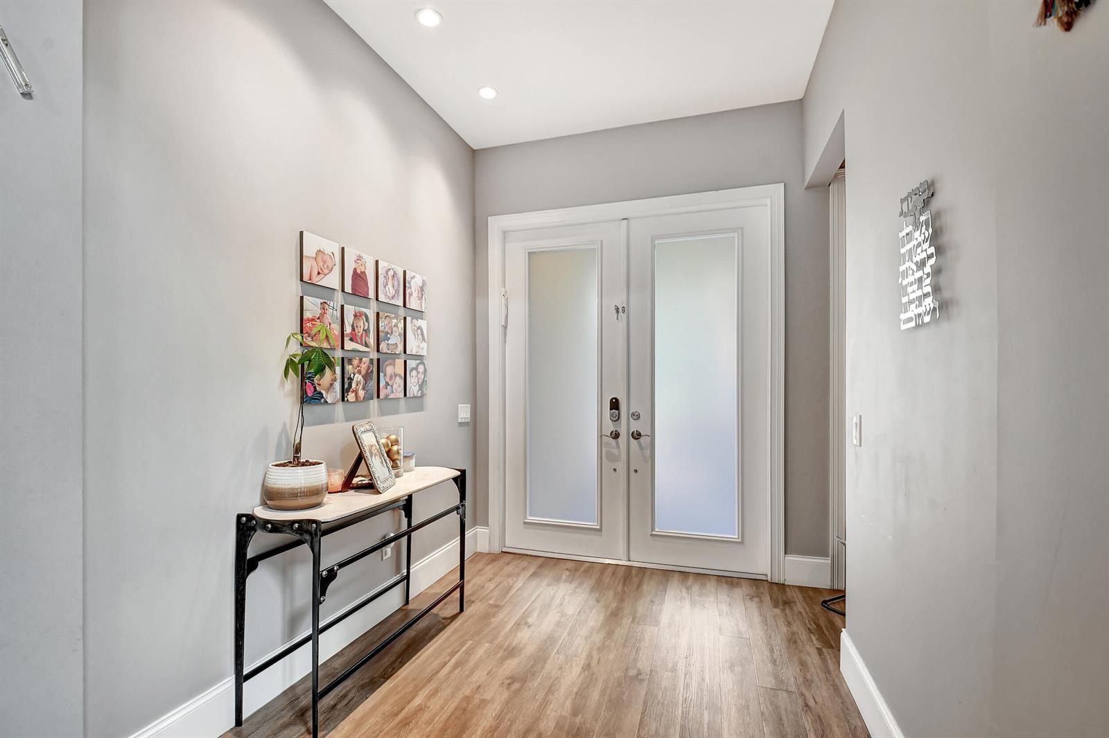 An entryway features light gray walls, wood-look flooring, a console table, and double glass doors — 16879 Bridge Crossing Circle, Delray Beach FL 33446, DELRAY BEACH, FL