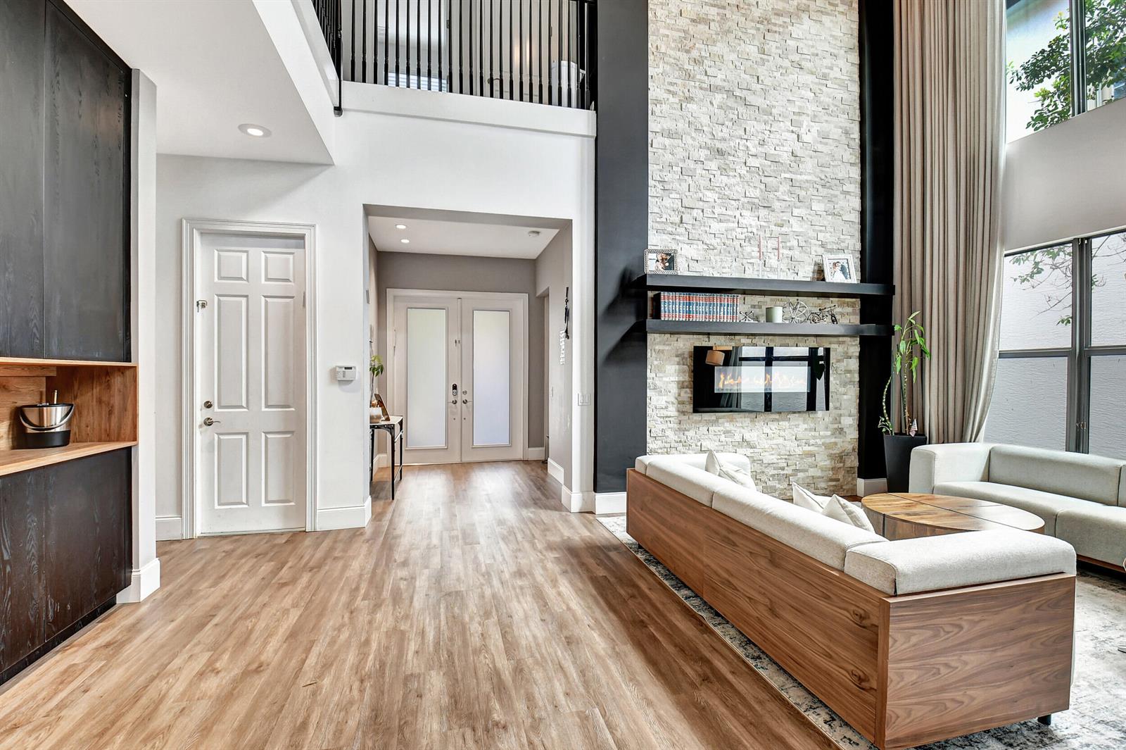A living room features a tall stone fireplace, wood flooring, and a view of the entryway — 16879 Bridge Crossing Circle, Delray Beach FL 33446, DELRAY BEACH, FL