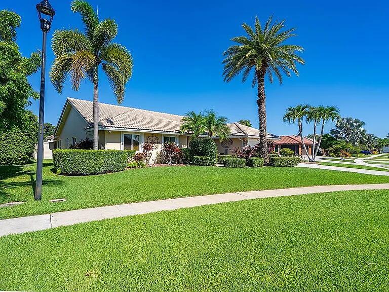 A single-story house with a tiled roof sits behind a manicured lawn and palm trees — 22373 Ensenada Way, Boca Raton FL 33433, BOCA RATON, FL