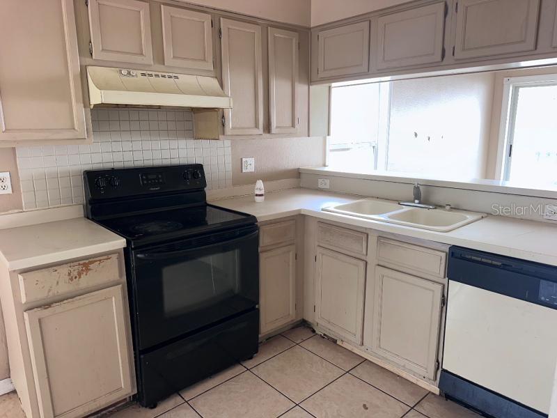 A kitchen features beige cabinets, a black stove, a white sink, and tile flooring — 1451 MOHRLAKE DRIVE, BRANDON, FL