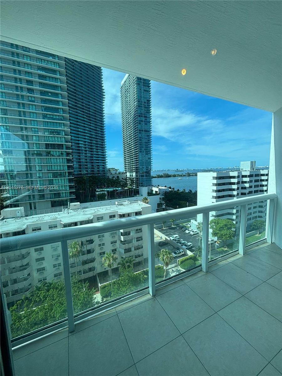 An empty room with dark hardwood floors features a balcony with a water view — 480 NE 30th St # 1004, Miami FL 33137, MIAMI, FL
