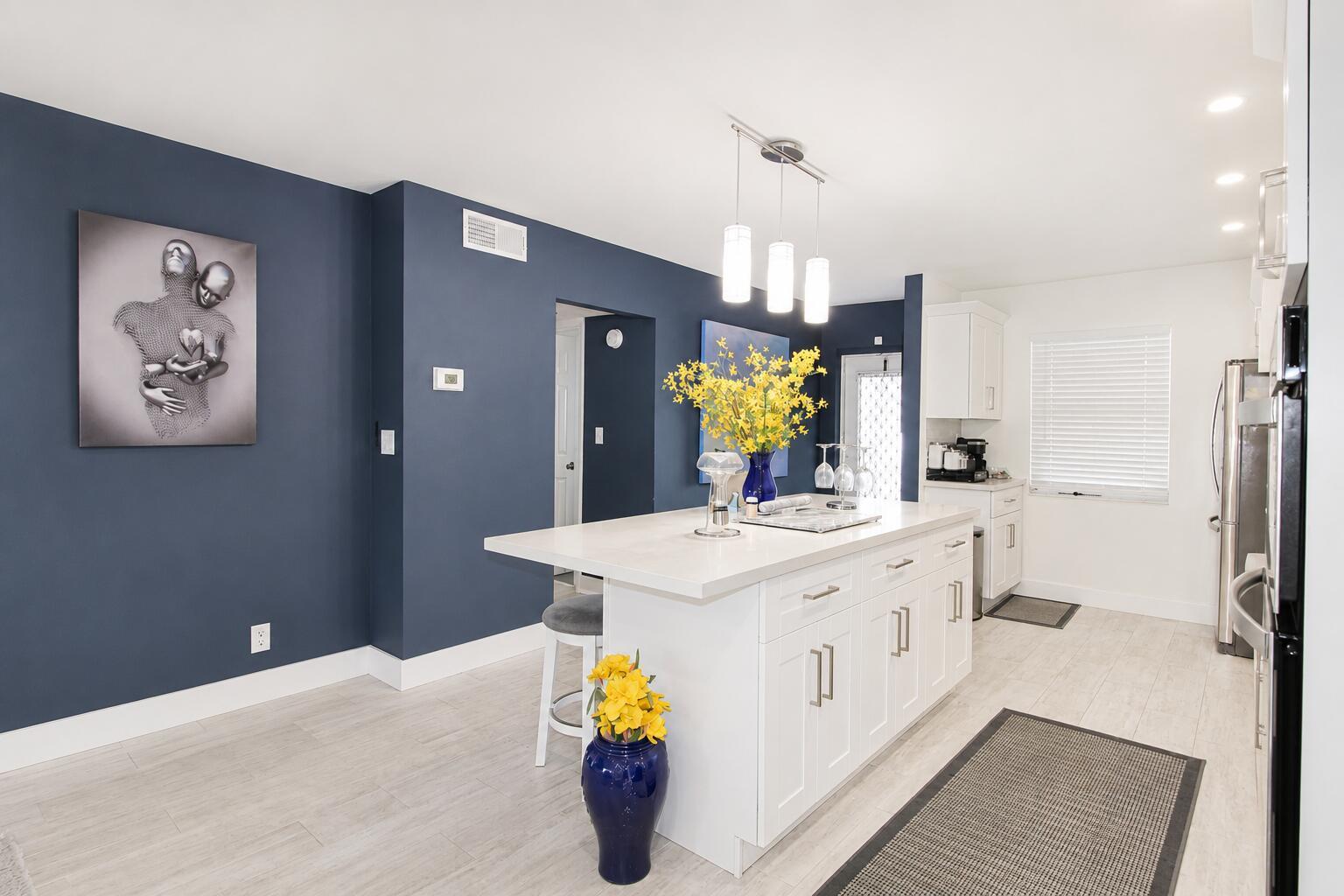 A modern kitchen features a white island, dark blue accent walls, and light wood-look flooring — 7787 Golf Cir Drive # 301, Margate FL 33063, MARGATE, FL