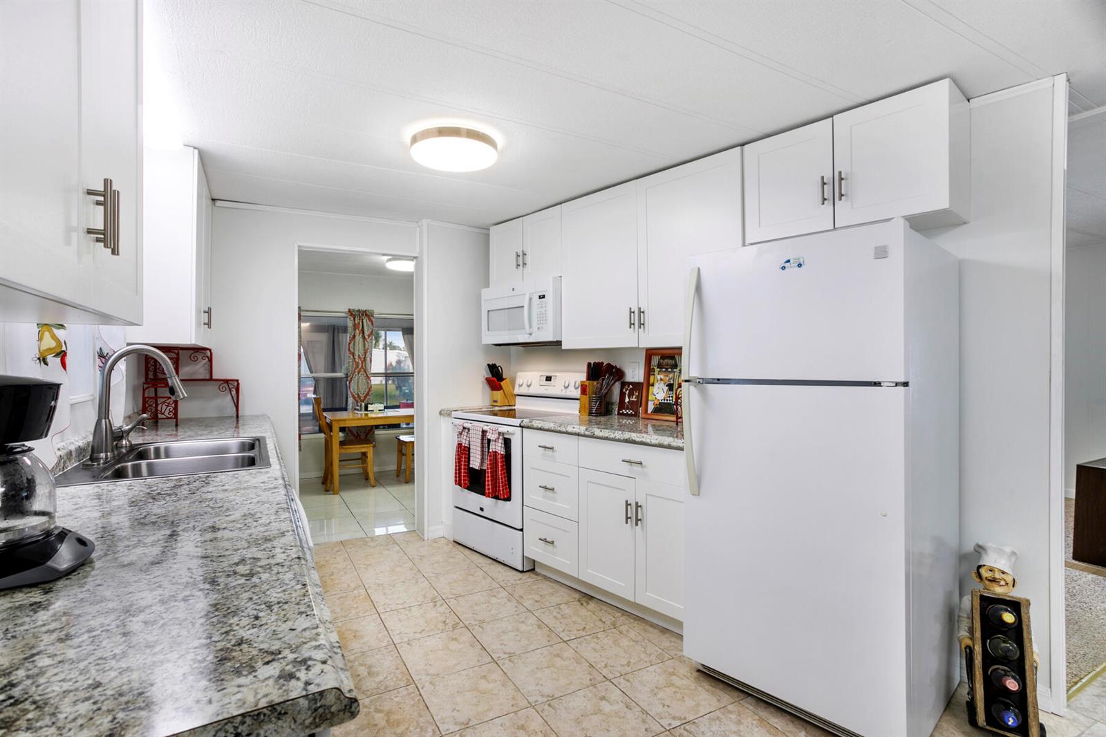 A kitchen features white cabinets, granite countertops, a white refrigerator, and tile flooring — 37026 Exuma Bay, Boynton Beach FL 33436, BOYNTON BEACH, FL